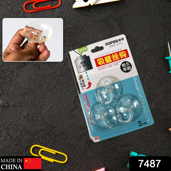 Retail packaging for three transparent suction cup hooks on a dark textured surface with office supplies.