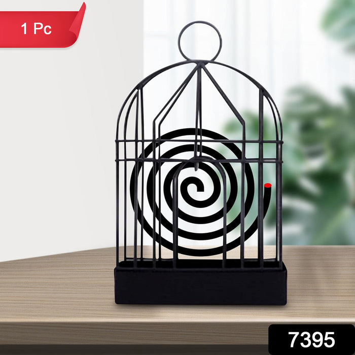 A black iron birdcage-style holder with a burning mosquito coil is on a wooden table, with a red