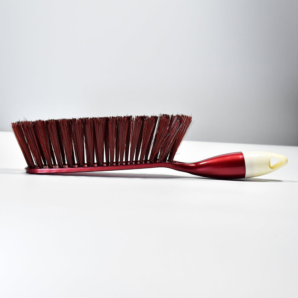 A red and white handled brush with brown bristles is shown from the side on a plain white background.