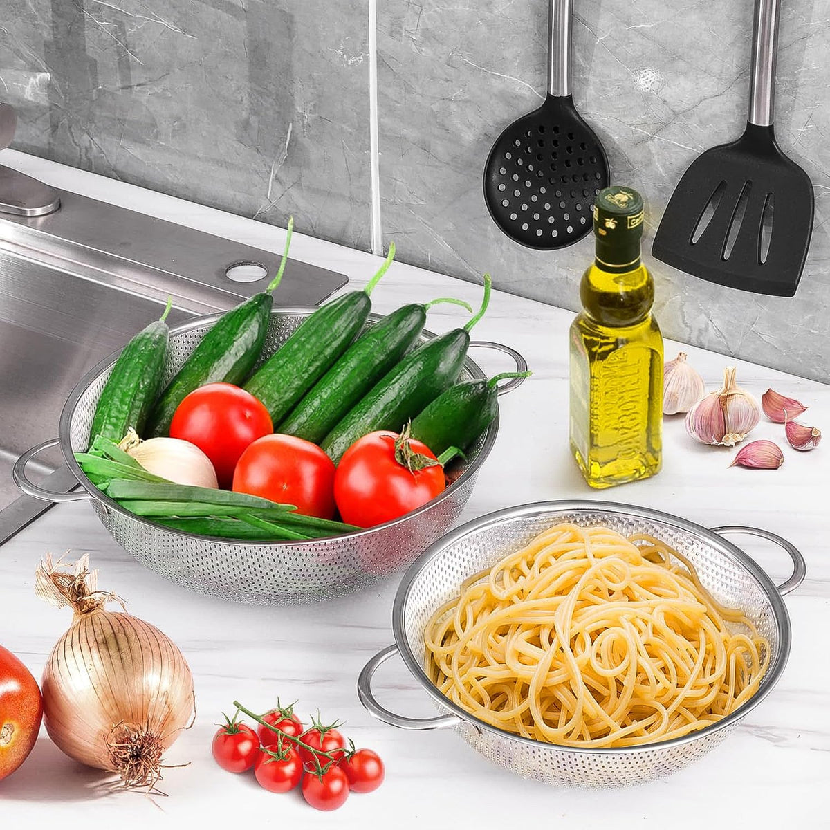 Two stainless steel strainer bowls, one with cucumbers and tomatoes, the other with pasta, on a kitchen counter.
