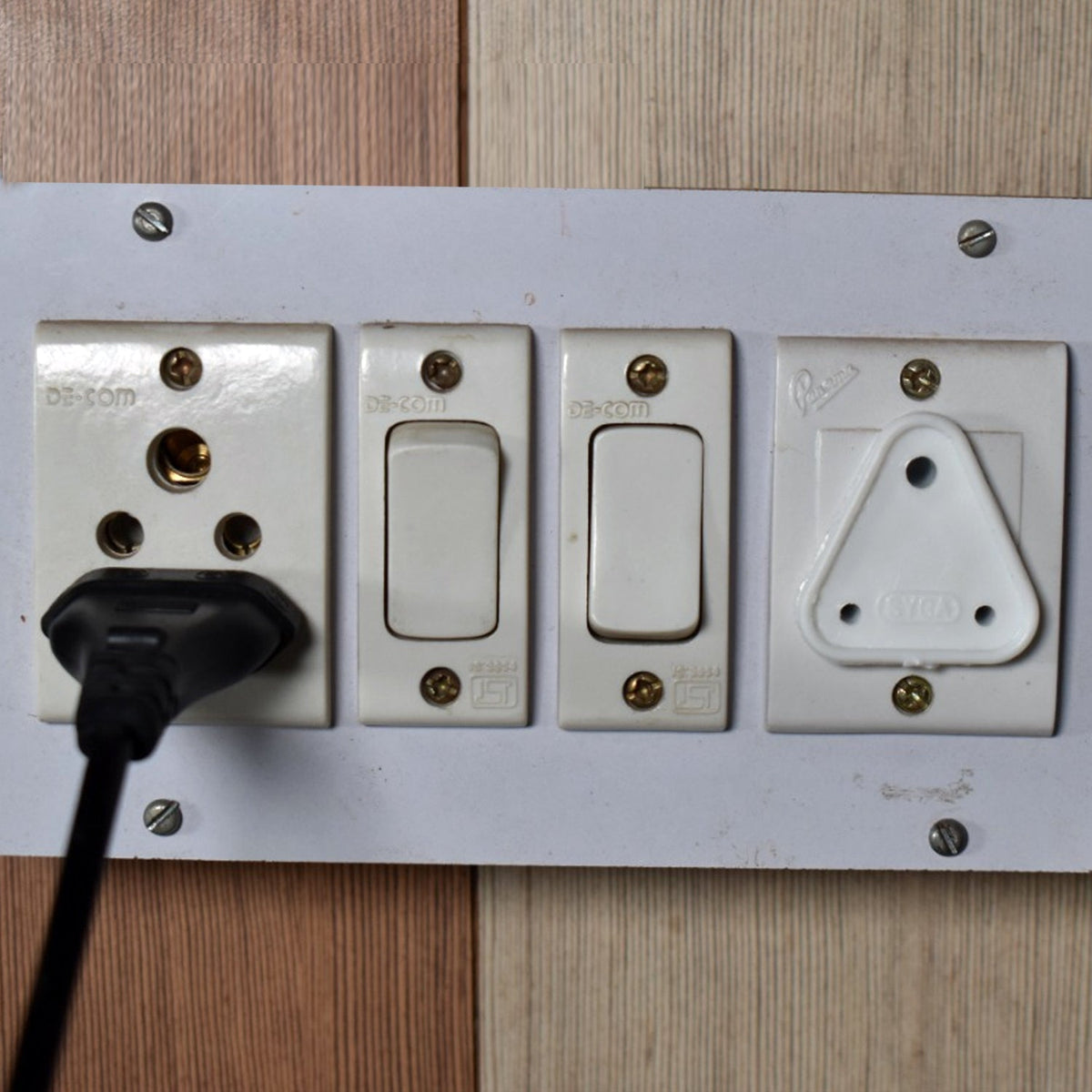A white plastic child safety socket cover installed in the rightmost socket of a white power strip on a wall.