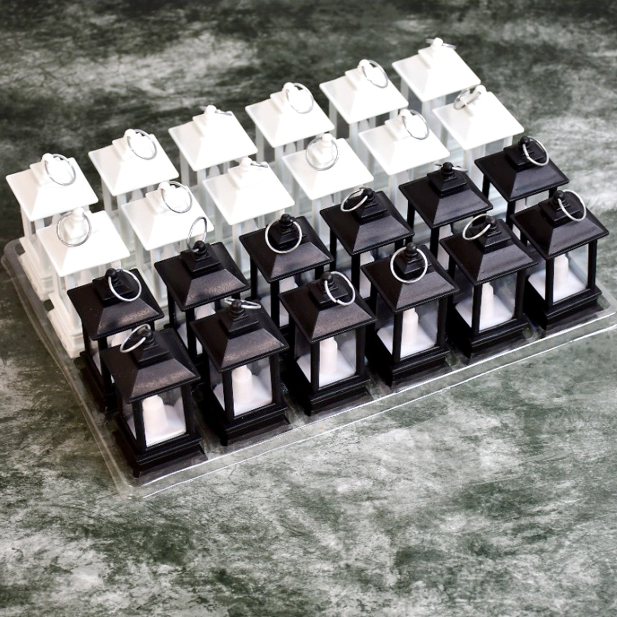 Twenty-four small black and white LED candle lanterns, arranged in rows on a clear plastic tray.