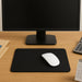 A black mouse pad with a white mouse on a wooden desk in front of a computer monitor.