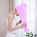 A woman with her head bent forward is about to put on a purple microfiber hair wrap, holding it open.