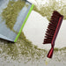 A red and white handled brush with brown bristles lies next to a gray dustpan, surrounded by green dried herbs.