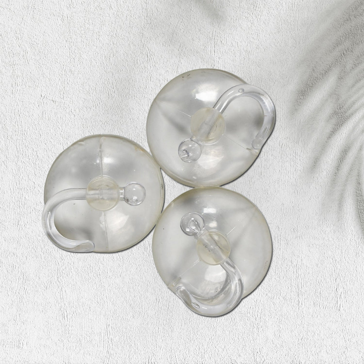 Three transparent suction cup hooks are arranged on a white textured surface with a subtle shadow.
