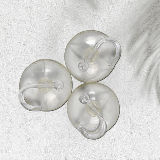 Three transparent suction cup hooks are arranged on a white textured surface with a subtle shadow.