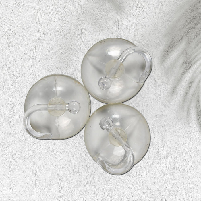 Three transparent suction cup hooks are arranged on a white textured surface with a subtle shadow.