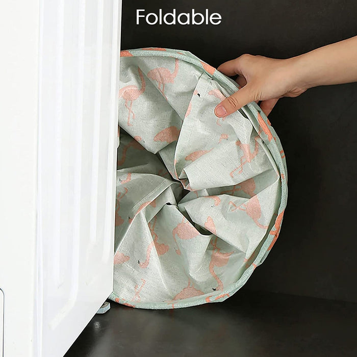 A hand compressing a flamingo-patterned fabric laundry hamper to demonstrate its foldable design, fitting into a narrow