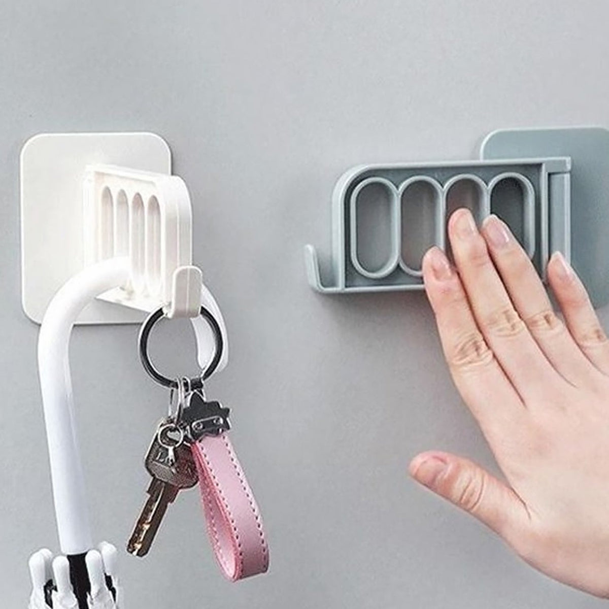 A hand touches a grey foldable wall hook, while a white one next to it holds an umbrella and keys.