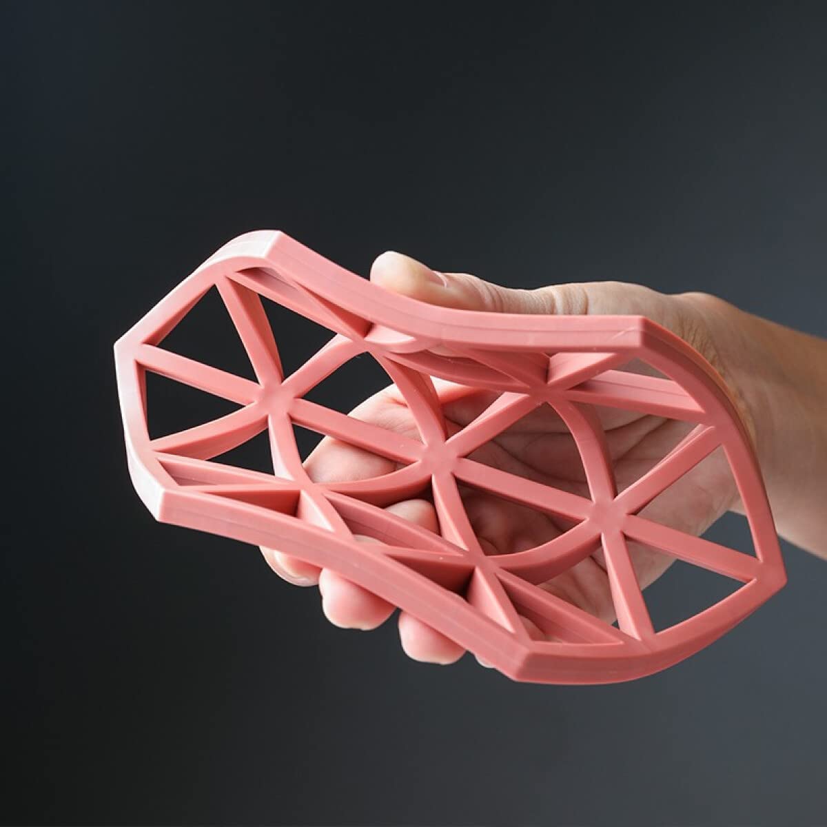 A hand holds and flexes a pink hexagonal silicone coaster, demonstrating its flexibility against a dark background.