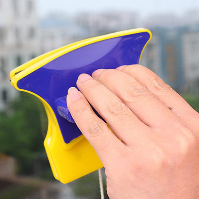 A hand holding and using the blue and yellow magnetic window cleaner on a glass surface.