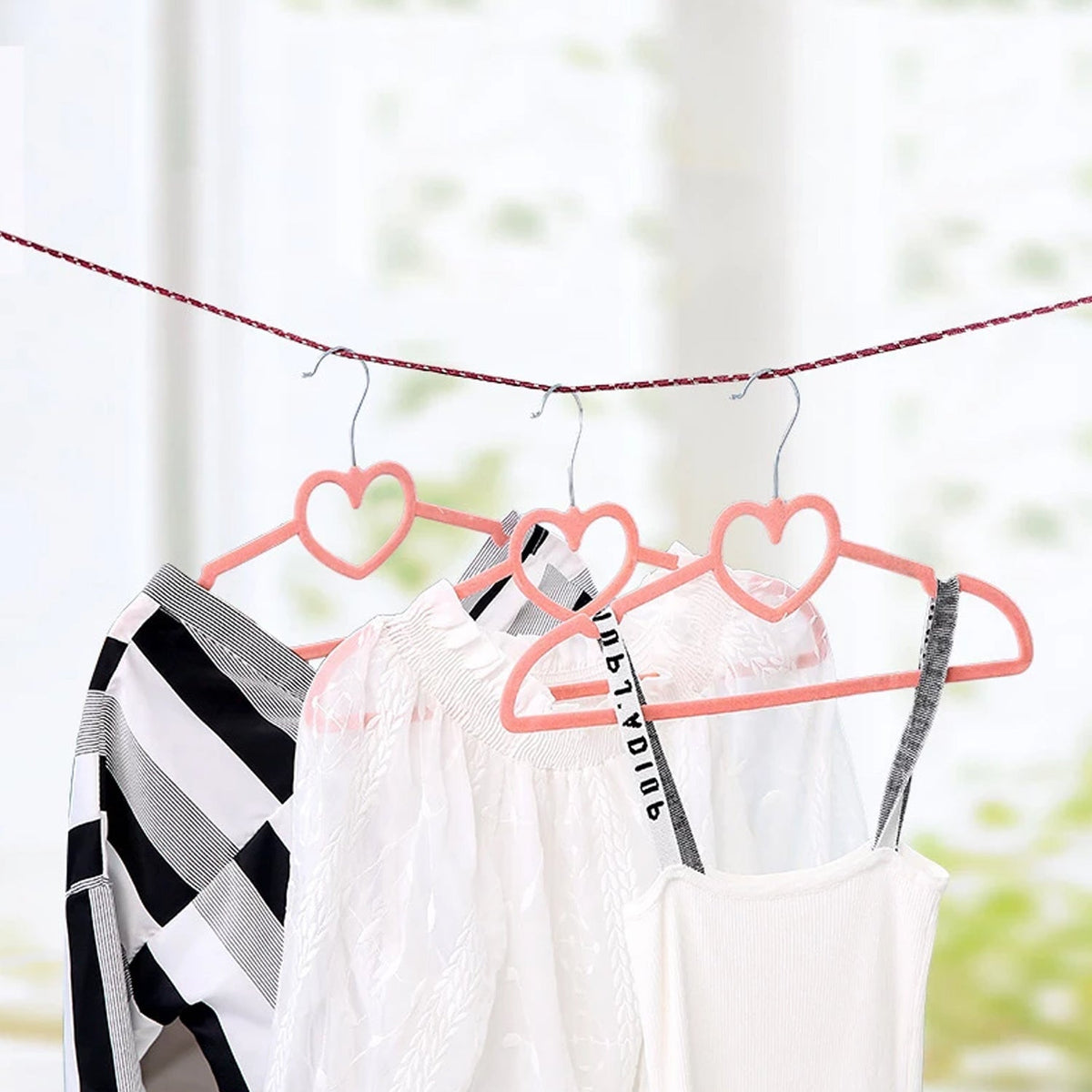 Pink heart-shaped hangers with clothes hanging on a red and white braided clothesline.