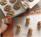 A hand in a colorful oven mitt next to cookie dough balls on baking paper and baked cookies on a tray.
