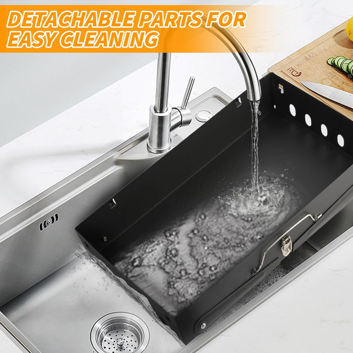 The black portable grill's ash tray being rinsed under a kitchen faucet in a stainless steel sink.