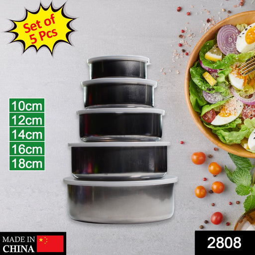 A set of five stacked stainless steel food containers with clear lids, showing size labels and a salad bowl in the