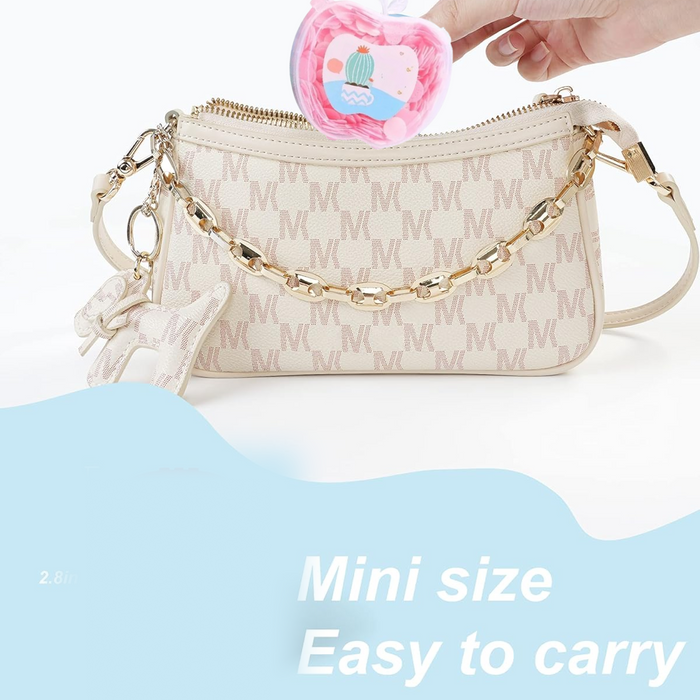 A hand places an apple-shaped soap container into a beige monogrammed handbag with a gold chain strap.