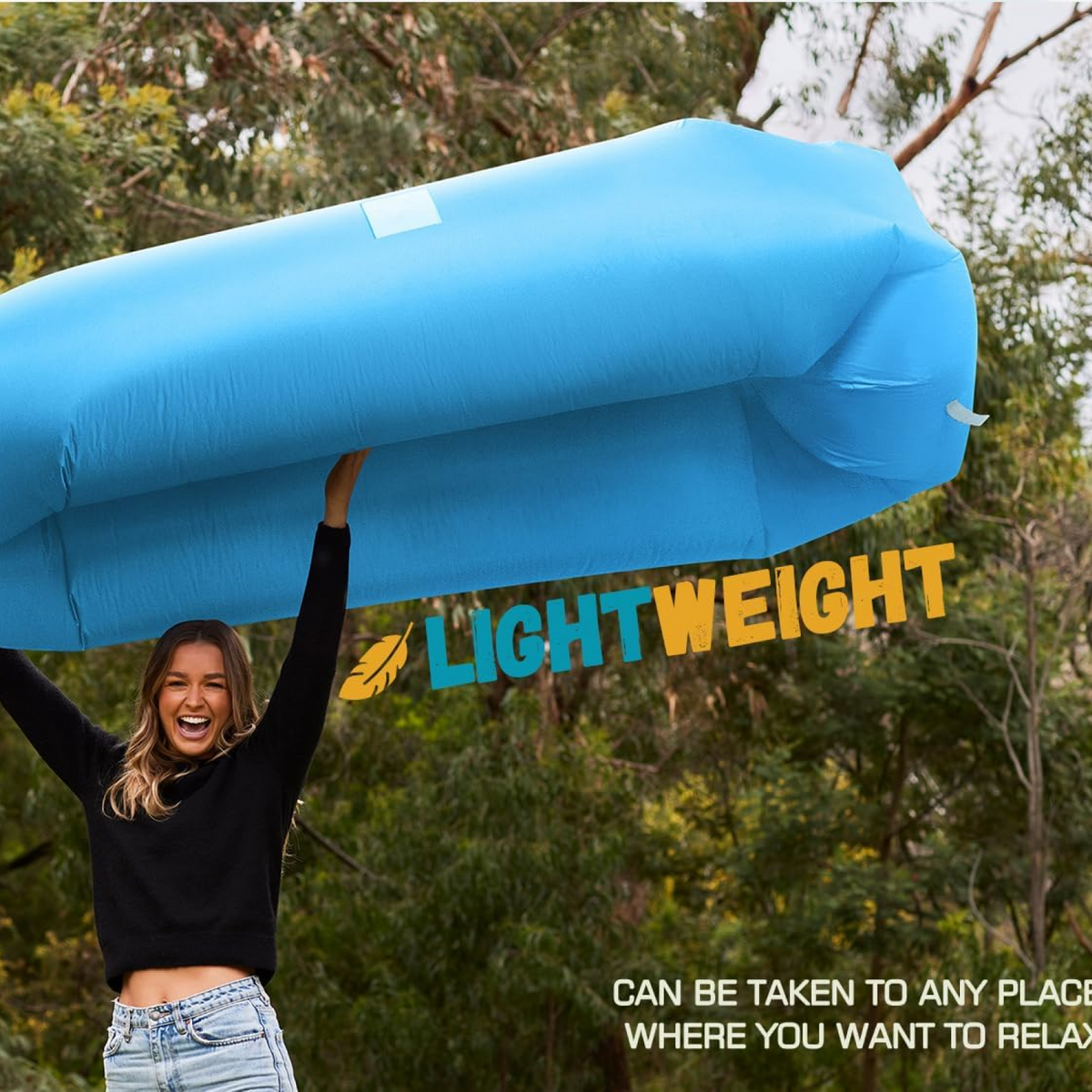A smiling woman holds up a lightweight blue inflatable lounger against a backdrop of green trees.