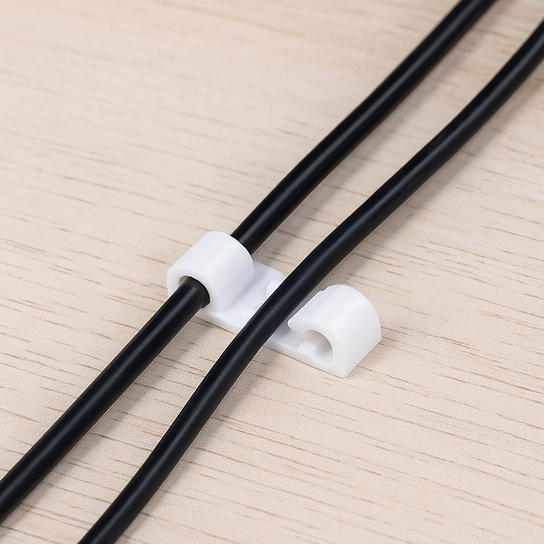 Two black cables are neatly secured side-by-side with a white self-adhesive clip on a light wooden surface.