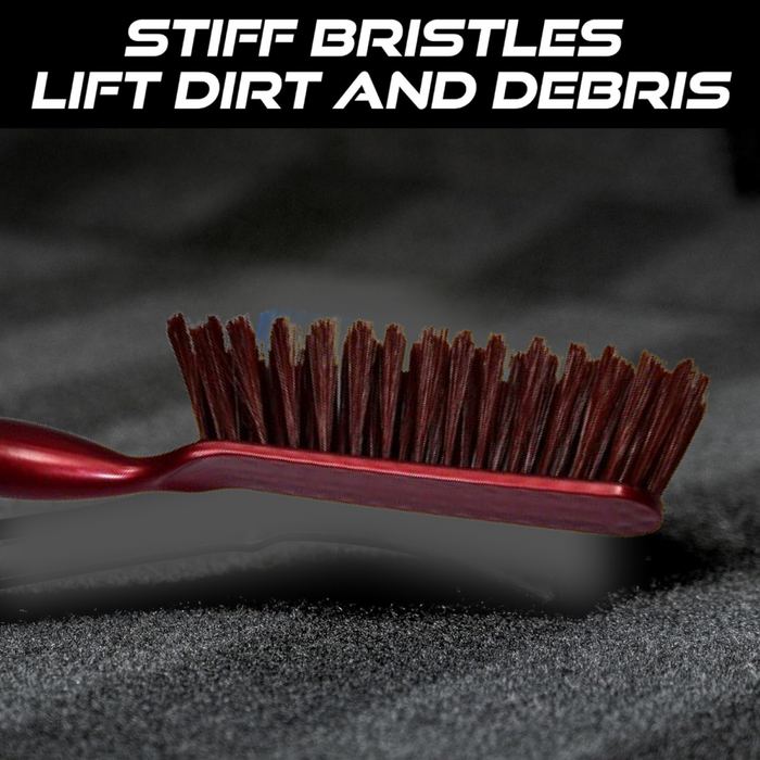 A close-up of the red and white handled brush with brown bristles on a dark textured surface, with text about stiff bristles.