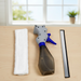 A white microfiber pad, a gray and blue spray bottle, and a silver squeegee blade arranged on a wooden table.