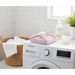 A pink microfiber hair towel wrap, folded into a square, sits on top of a washing machine next to a laundry basket and