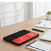A black and red laptop sleeve rests on a wooden desk with a pen and notepad nearby.