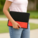 A person holds a black and red mesh laptop sleeve against their hip outdoors.