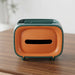 Green and orange rectangular tissue box with a wide opening on a wooden table.