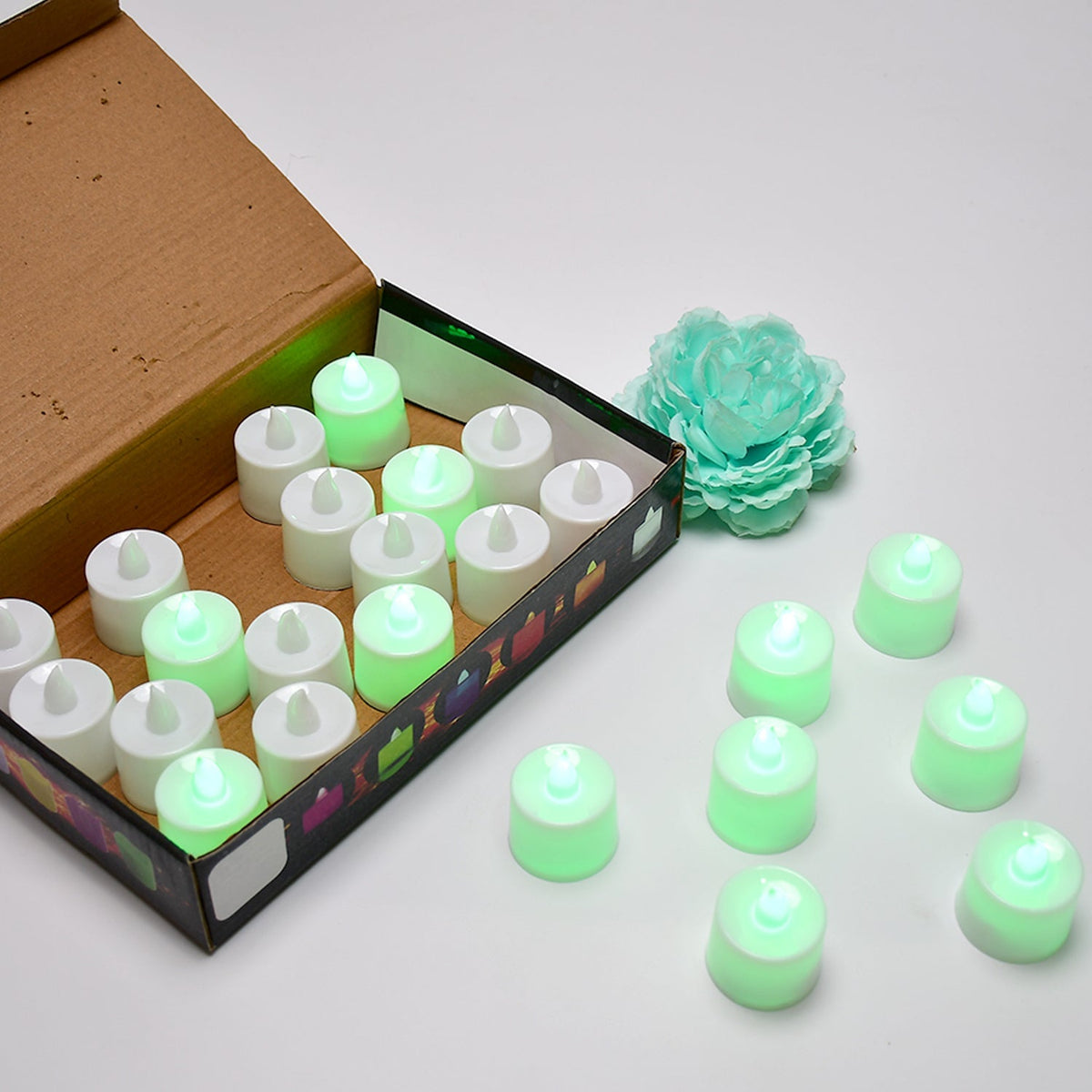 An open brown box contains twenty-four white flameless LED tealights, with several more glowing tealights on the white table.