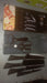Six-piece black serrated knife set with peeler and scissors in their packaging, next to a box with fruit images.