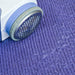 Close-up of a blue and white lint remover removing fuzz from a purple knitted fabric.