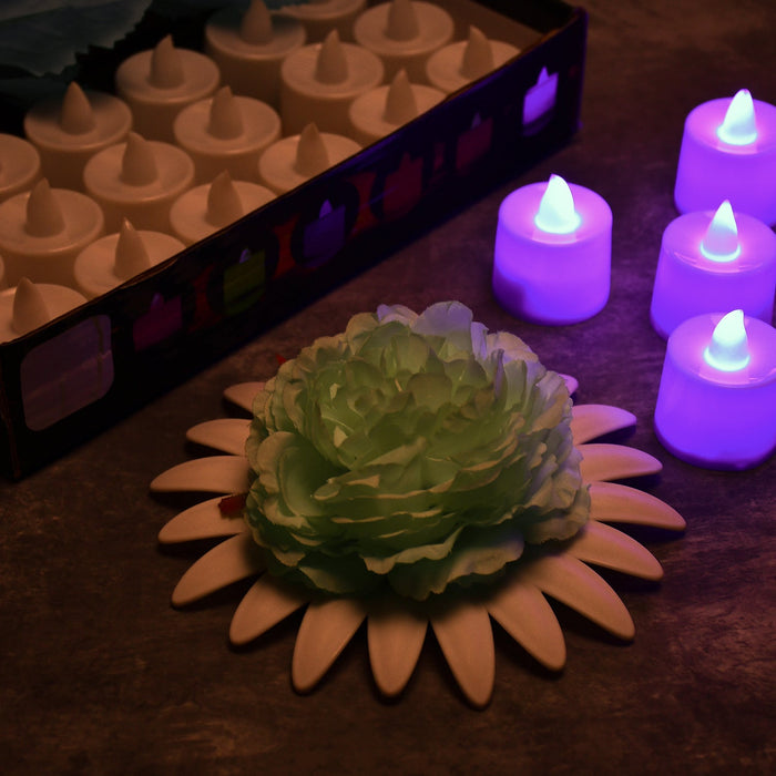 A box of white LED tealights, several purple glowing tealights, and a light green flower on a white base.