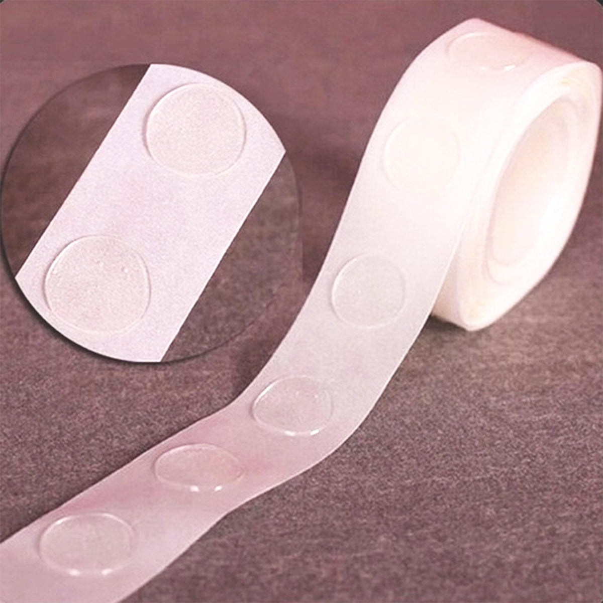 A close-up of a roll of clear, round glue dots on a white paper backing, with a magnified view in a circular inset.