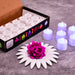 A box of white LED tealights next to several purple glowing tealights and a pink rose on a white flower-shaped base.