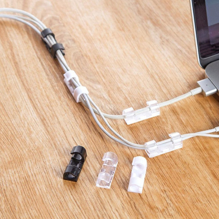 Various black, clear, and white cable clips organize grey cables on a wooden desk next to a laptop.