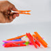 A hand holds an orange plastic clothes clip above a small pile of other colorful clips on a white background.