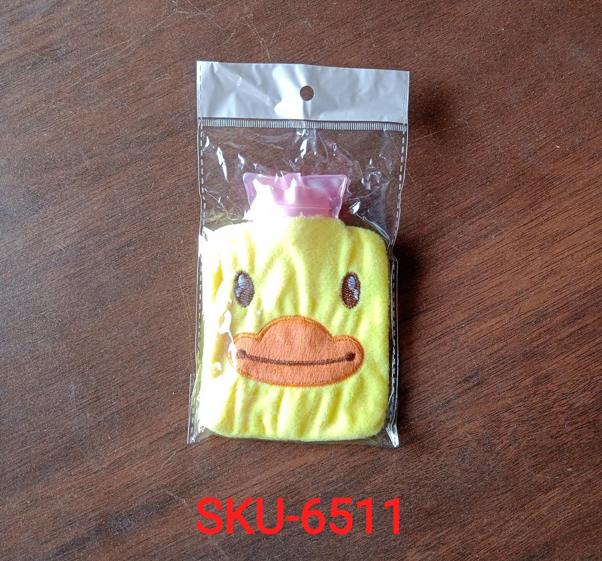 A yellow duck hot water bottle in a clear plastic bag with a white top, on a wooden surface.