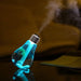 A blue bulb-shaped humidifier with palm trees inside emits mist, reflecting on a dark surface.
