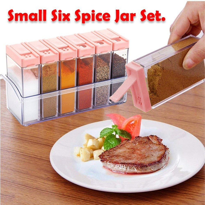 A hand sprinkling spices from a pink-lidded jar onto a cooked steak with potatoes and tomatoes on a white plate.