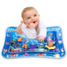 A baby in a white long-sleeve onesie smiles while doing tummy time on a blue water play mat.