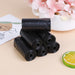 Six rolls of black garbage bags stacked on a table with a floral arrangement and decorative card.