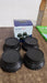 Four black round washing machine support legs are displayed in front of a blue and white product box on a wooden surface.