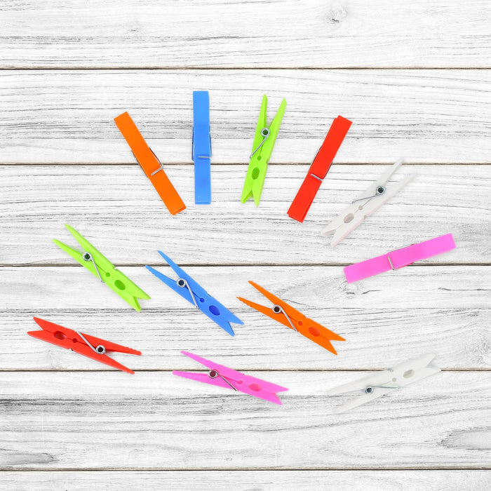 Ten colorful plastic clothes clips scattered on a white wooden background, showcasing different colors.