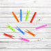 Ten colorful plastic clothes clips scattered on a white wooden background, showcasing different colors.