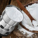 The grinder's stainless steel bowl is filled with white flour, next to a wooden bowl of flour and a spoon.