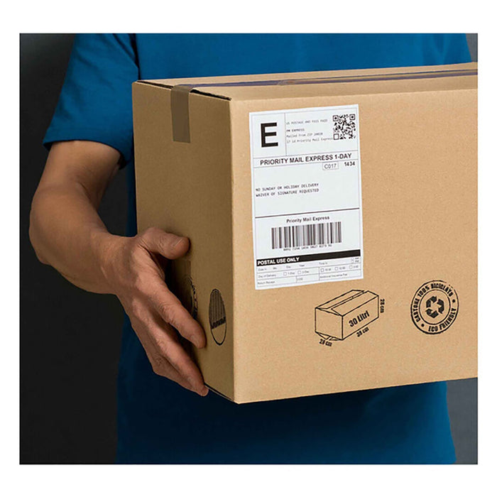 A person in a blue shirt holds a brown cardboard box with a large white shipping label affixed to its side.