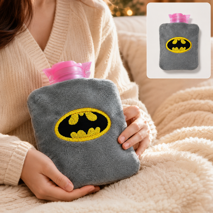 Person holding a gray plush hot water bag with a yellow and black Batman logo. A smaller inset shows the bag alone.