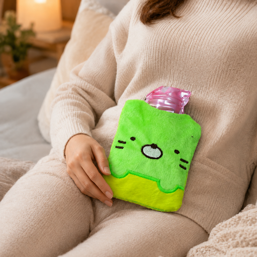 A person in a cream sweater holds a green and yellow kitty hot water bag on their stomach.