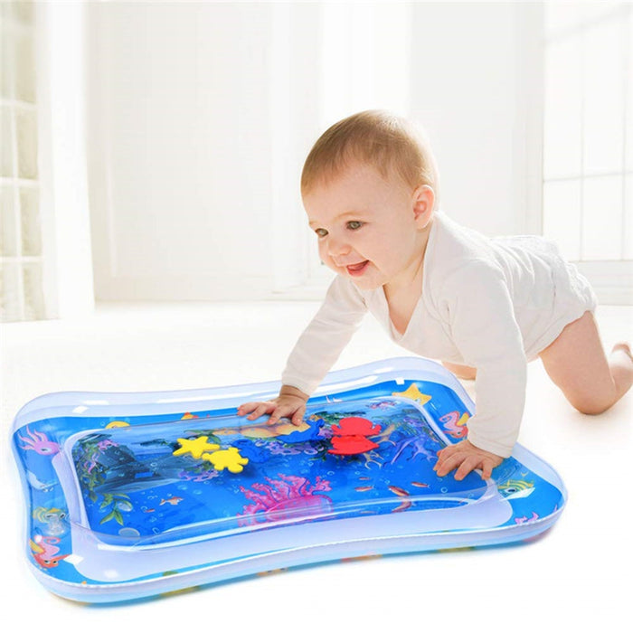 A baby in a white onesie crawls on a blue inflatable water mat with colorful floating toys.